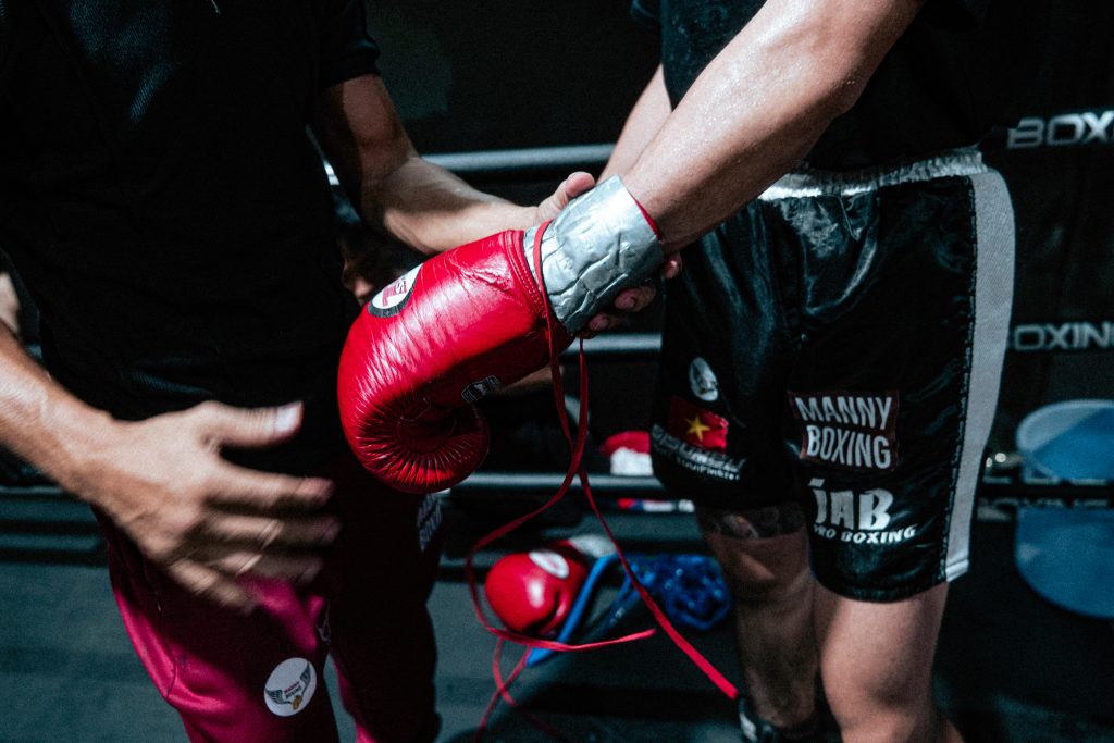 Un entraîneur aide un boxeur à enfiler son gant de boxe rouge avant un combat, dans une salle de boxe professionnelle.